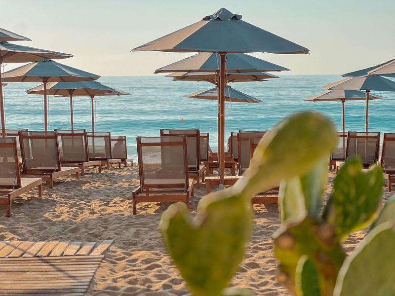 Plážová lehátka a slunečníky na písečné pláži s výhledem na moře při západu slunce.