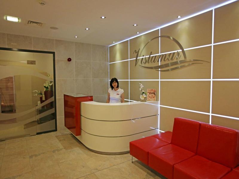 Moderní hotelová recepce s bílým pultem a červenou pohovkou v světlé hale.