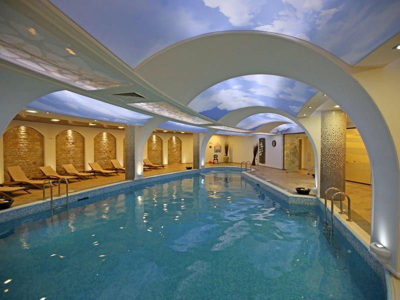 Luxusní krytý bazén s klenutými oblouky, lehátky a teplým osvětlením.