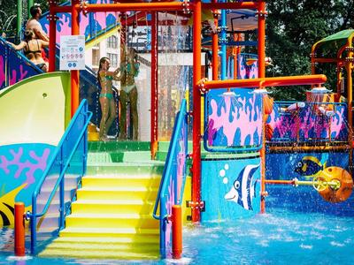 Bunter Wasserspielplatz mit Rutsche, Treppen und spritzenden Wasserfontänen.