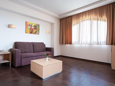 Modern hotel living area with purple sofa, small table, and large curtained windows.