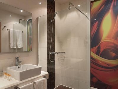 Modern hotel shower with glass partition, washbasin, and colorful wall decoration.