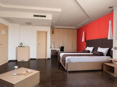 Modern hotel room with two beds, red accent wall, and dark flooring.