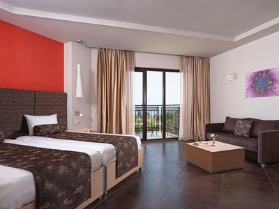 A modern hotel room with two beds, sofa, coffee table, and balcony view.