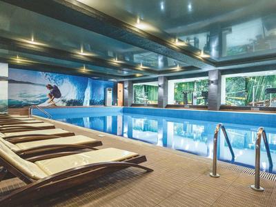 Modern indoor pool with lounge chairs and large windows offering views of nature.