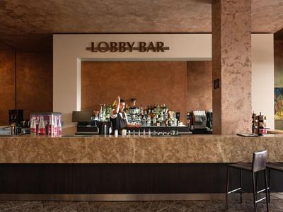 Simple hotel lobby bar area with counter, bar stools, and various drinks.