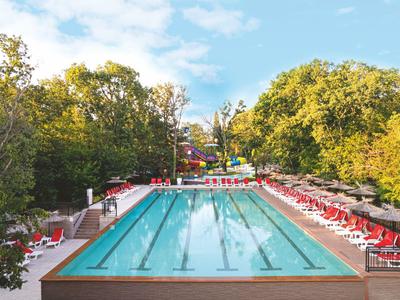 Outdoor swimming pool with blue water, surrounded by red lounge chairs and trees.