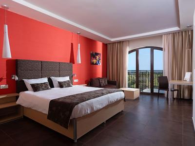 Modern hotel room with large bed, red walls, and balcony overlooking greenery.