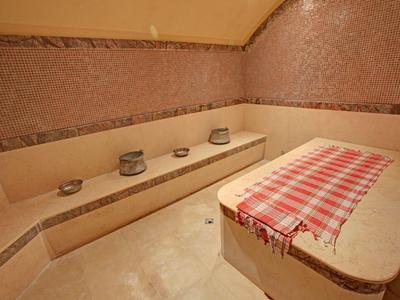 Ein traditioneller Hammam mit roten Fliesen, Sitzbank und Tisch mit rot kariertem Tuch.