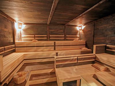 Holzsauna mit mehrstufigen Sitzbänken, zwei Wandlampen und einem Holzeimer auf dem Boden.