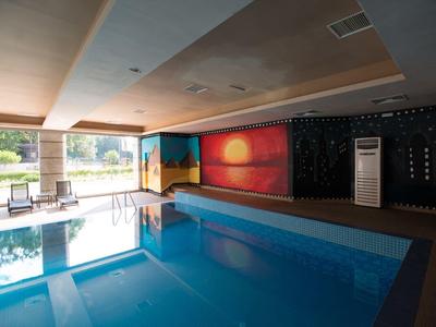 Innenpool mit ruhigem Wasser, Sonnenuntergang-Wandbild und großen Fenstern zum Garten.