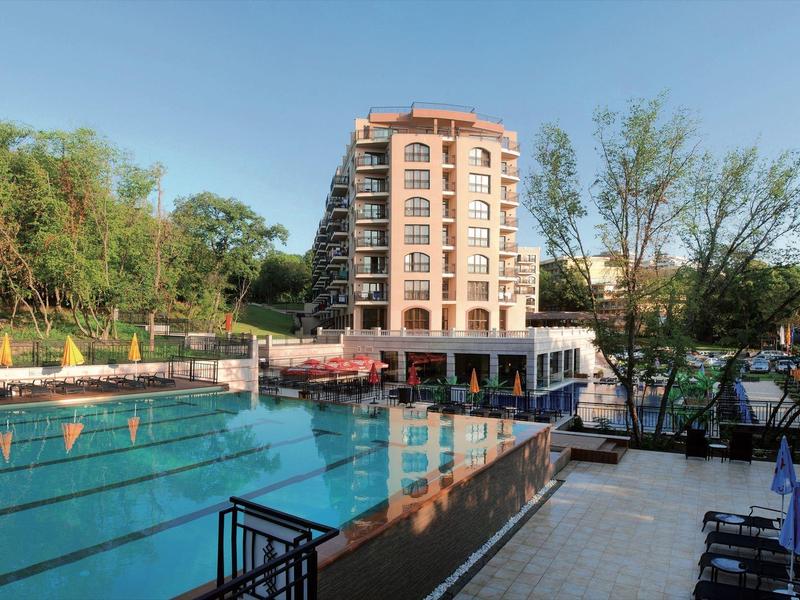 Großes Hotelgebäude neben einem Freibad mit Schwimmerbahnen und Sonnenterrasse.