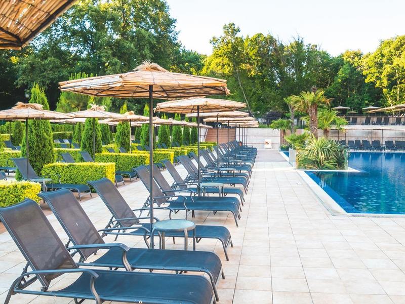 Poolbereich mit Sonnenschirmen und Liegestühlen in einer Hotelanlage bei Tageslicht