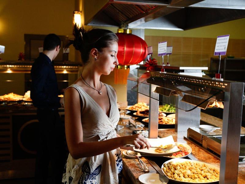 Frau bedient sich am Buffet mit verschiedenen warmen Speisen in gemütlicher Restaurant-Atmosphäre.
