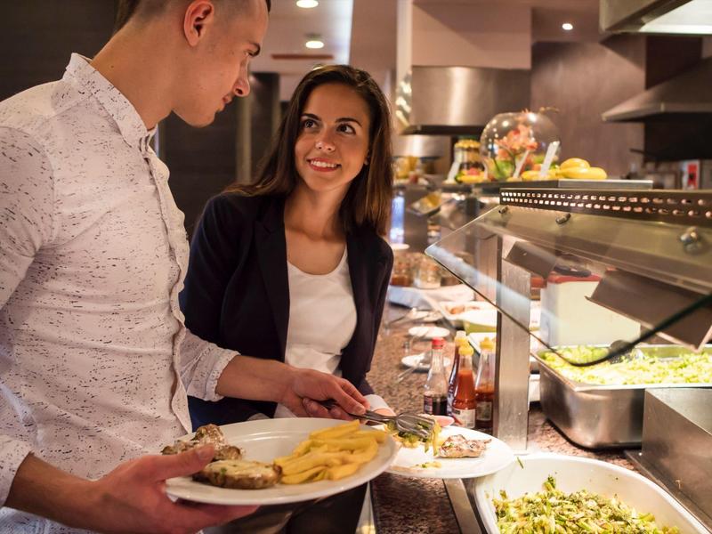 Zwei Personen wählen Speisen an einem Buffet in einem Restaurant oder Hotel.