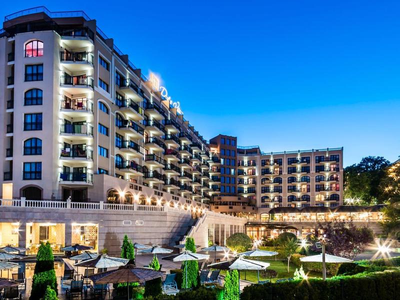 Modernes Hotelgebäude bei Dämmerung mit beleuchteten Balkonen und gepflegtem Garten