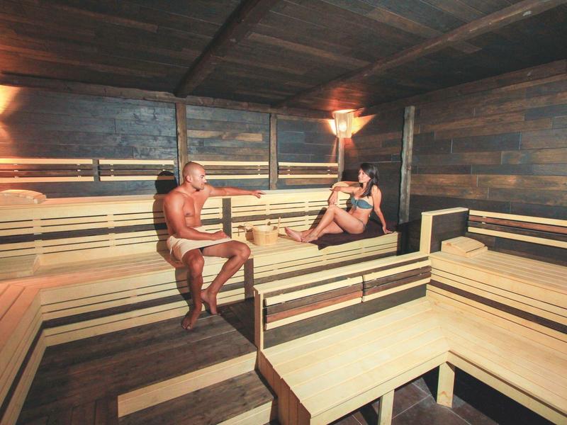 Zwei Personen entspannen in einer Holzbanksauna mit gedämpftem Licht.