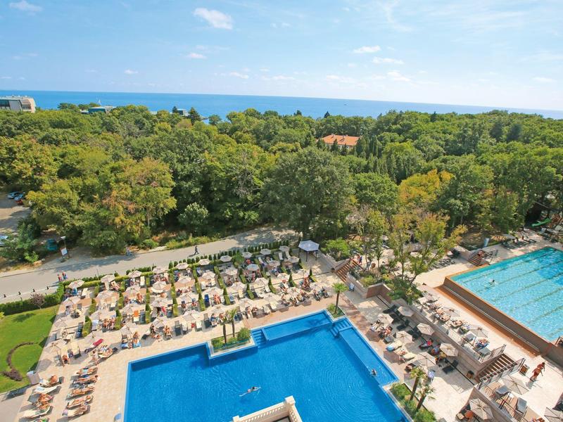 Großer Außenpoolbereich mit Liegestühlen und Sonnenschirmen neben einem Wald und Blick auf das Meer