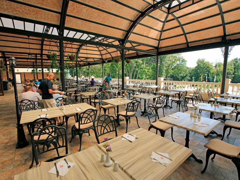 Überdachter Außenbereich eines Restaurants mit Holztischen und Blick auf Bäume.