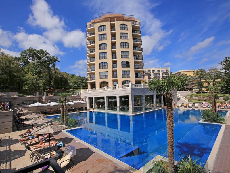 Luxushotel mit Außenpool, Sonnenliegen und blauem Himmel in einer grünen Umgebung.