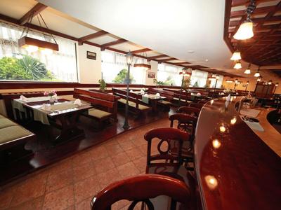 Großes Restaurant mit Holztischen, grünen Sitzbänken und warmem Deckenlicht in hellem Ambiente.