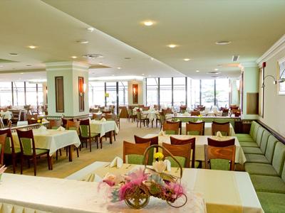 Ampia sala da pranzo con tavoli apparecchiati, tovaglie bianche e composizioni floreali.