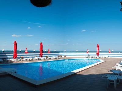 Außenpool mit blauer Wasseroberfläche, roten Sonnenschirmen und weißem Poolbereich unter blauem Himmel.