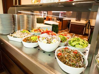Buffet mit verschiedenen frischen Salaten in weißen Schüsseln und Tellerstapeln auf einem Metalltisch.
