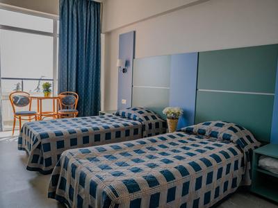 Zwei Einzelbetten mit blau karierten Decken, neben Fenster mit blauen Vorhängen und orangenen Stühlen.