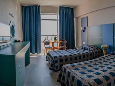 Ein helles Hotelzimmer mit zwei Betten, blau gemusterten Vorhängen und modernem Mobiliar.