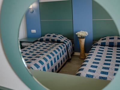 Zwei Betten mit blau-weiß karierten Decken, Spiegel und Vase mit weißen Blumen im Zimmer.