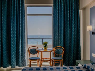 Hell beleuchtetes Zimmer mit blau gemusterten Vorhängen, zwei Holzstühlen und kleinem Tisch am Balkon.