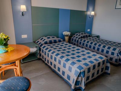 Zwei Einzelbetten mit blau karierten Decken in schlichtem, modernem Zimmer mit Holzstuhl und Tisch.