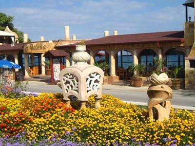 Bunte Blumenbeete mit zwei verzierten Steinskulpturen vor einem Gebäude mit Bogenfenstern.