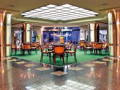 Ein moderner, heller Sitzbereich mit grünen Teppichen, Holzstühlen und glänzendem Marmorboden.