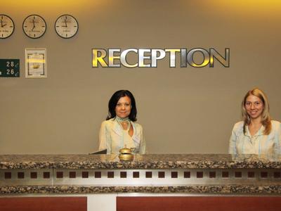 Due receptionist sono dietro al banco con un'insegna RECEPTION e tre orologi sulla parete.