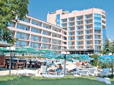 Großes Hotel mit mehreren Etagen, Sonnenschirmen und Liegestühlen vor dem Gebäude auf Grasfläche.