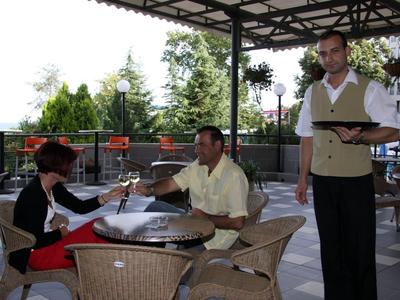 Tavolo apparecchiato sulla terrazza con cameriere e clienti sotto il sole