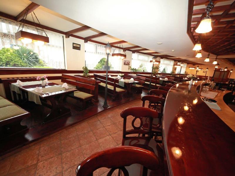 Großes Restaurant mit Holztischen, grünen Sitzbänken und warmem Deckenlicht in hellem Ambiente.