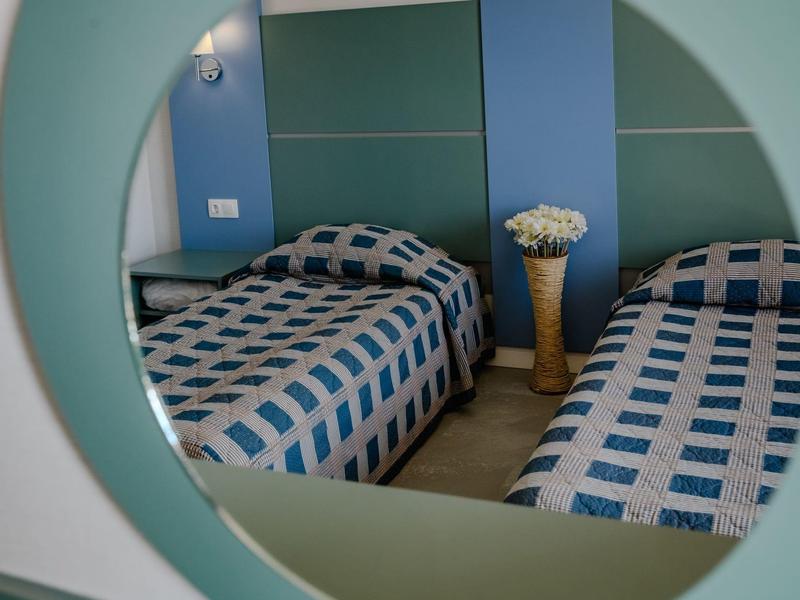 Zwei Betten mit blau-weiß karierten Decken, Spiegel und Vase mit weißen Blumen im Zimmer.