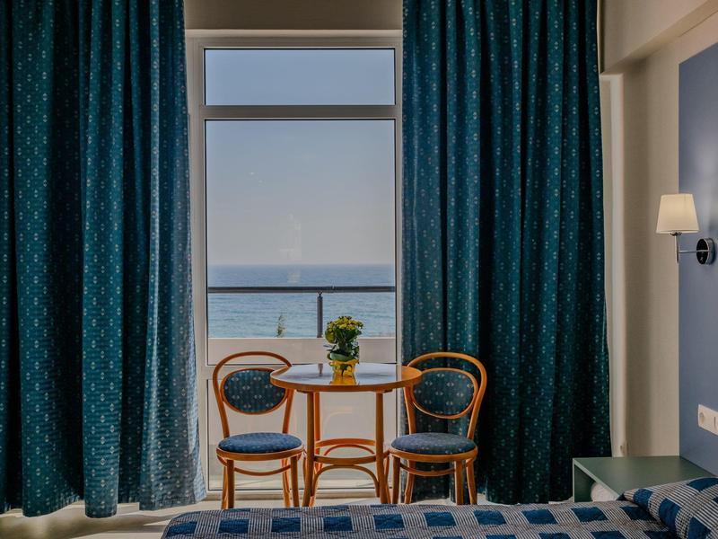 Hell beleuchtetes Zimmer mit blau gemusterten Vorhängen, zwei Holzstühlen und kleinem Tisch am Balkon.