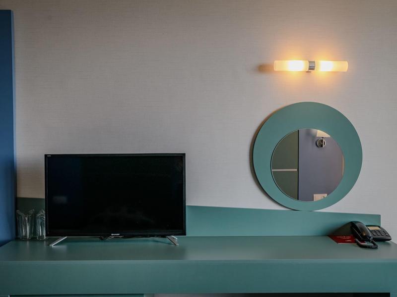 Moderner Raum mit flachem Fernseher, rundem Spiegel, türkisfarbenem Möbel und Wandlampe.