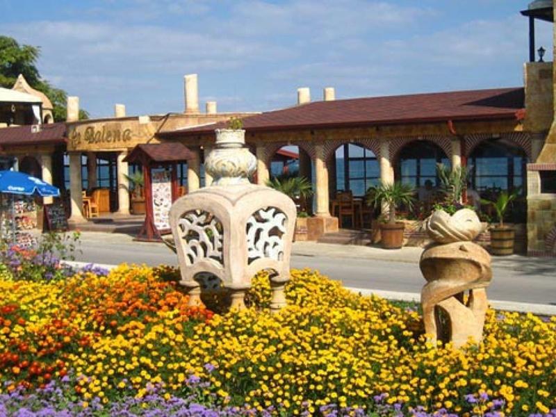Bunte Blumenbeete mit zwei verzierten Steinskulpturen vor einem Gebäude mit Bogenfenstern.