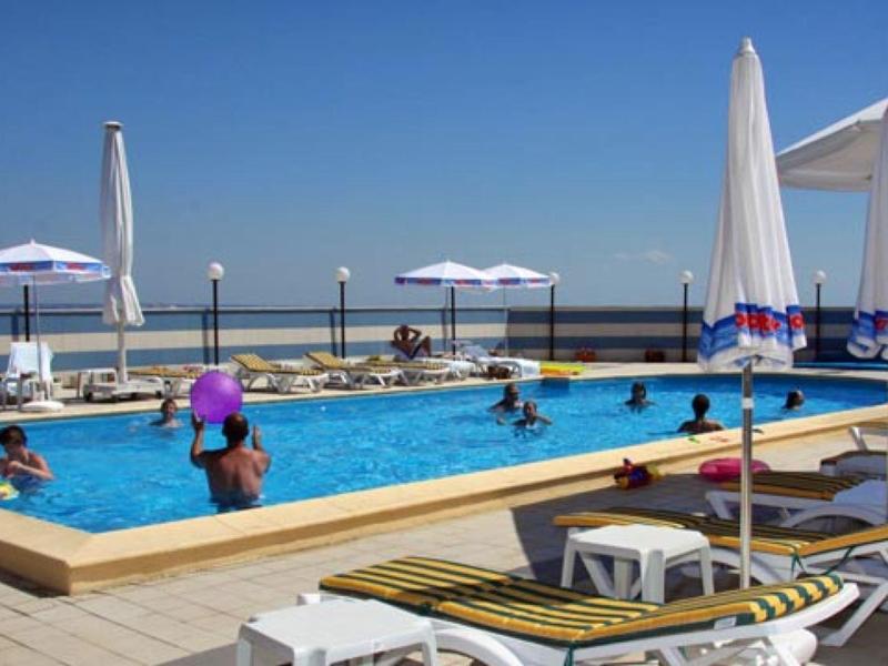 Ein Außenpool mit Liegestühlen und Sonnenschirmen bei klarem Himmel am Meer.