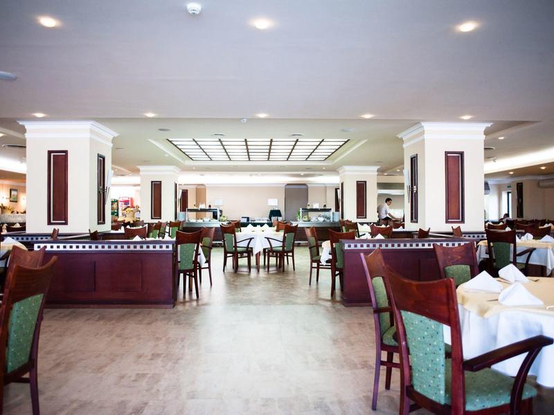 Großer, heller Speisesaal mit Holzböden, weißen Tischdecken und grünen Stühlen.