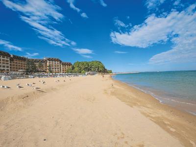 Large plage de sable avec des gens, ciel bleu et hôtels en arrière-plan au bord de la mer.