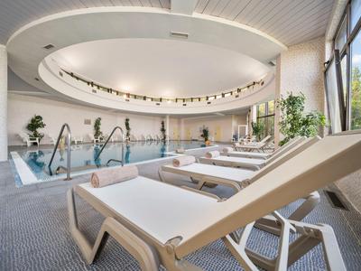 Bright indoor pool with lounge chairs and large windows overlooking trees.