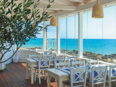 Restaurant lumineux avec meubles en bois blanc et vue sur la mer à travers de grandes fenêtres.