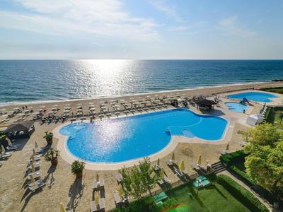 Large pool with sun loungers on the beach, sea and sky in the background under clear sun.
