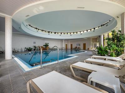 Modern indoor pool with lounge chairs and plants under a large circular ceiling.